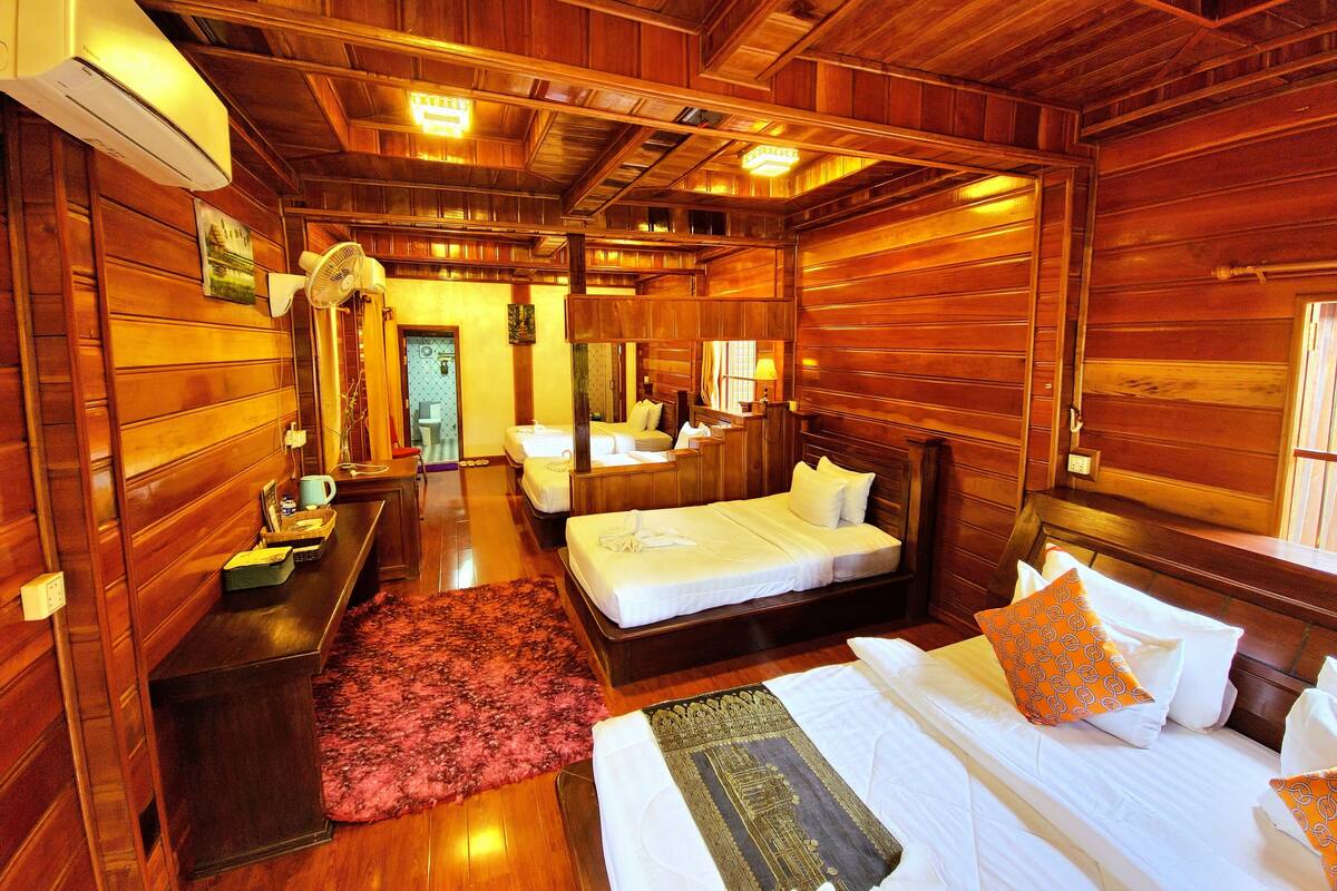 A wooden cabin room with two beds, a desk, a mirror, and a window.