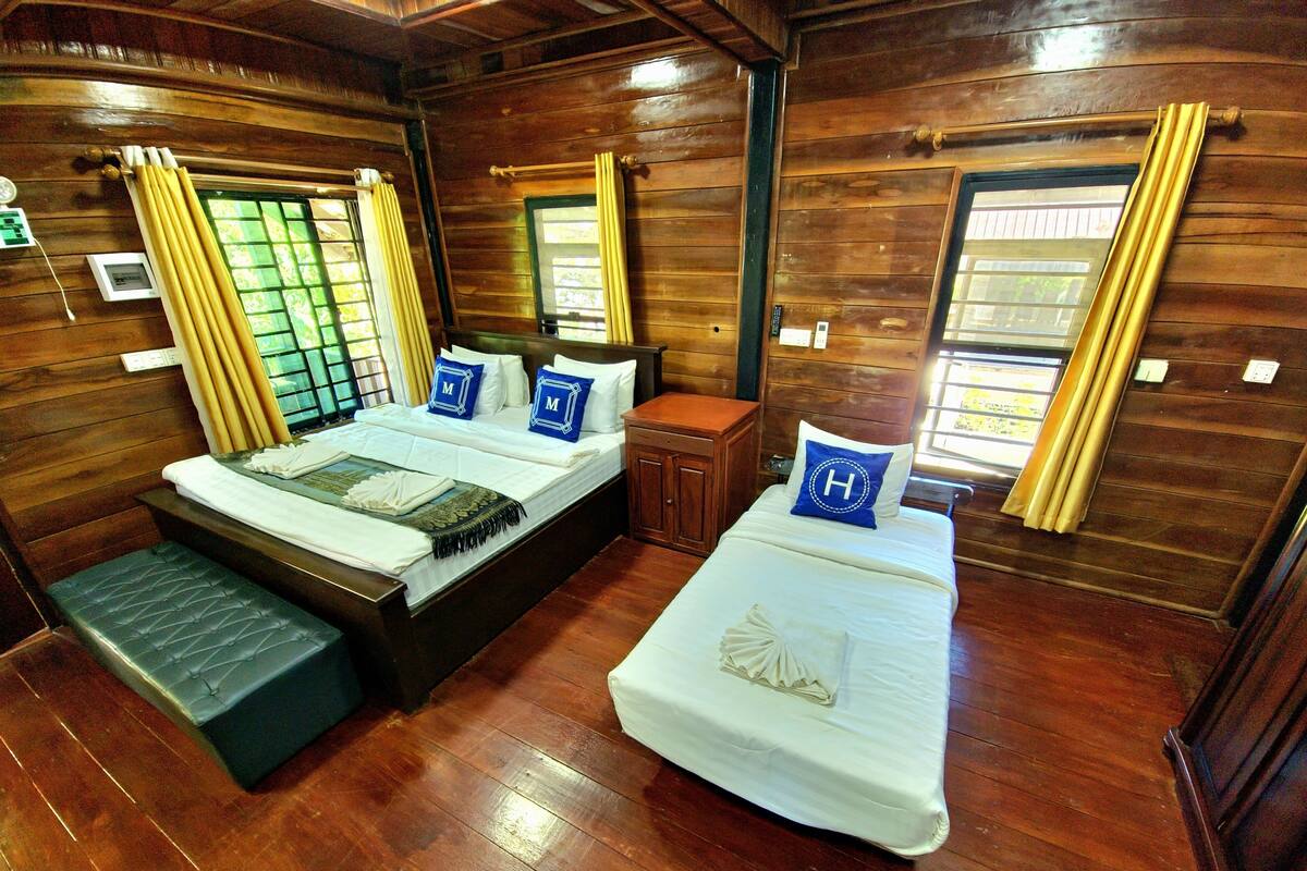 A wooden cabin-style room with two beds, a bench, and a small table.