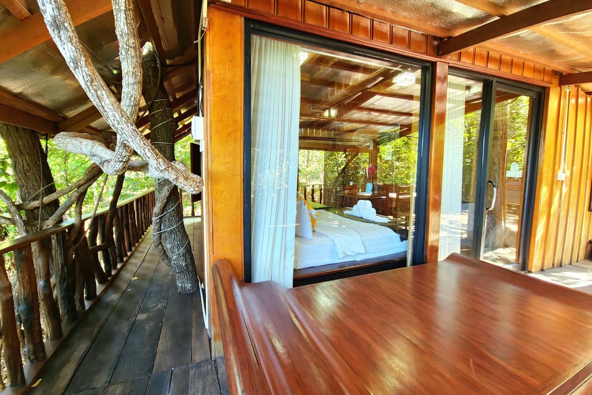 A wooden cabin with a bed, a bench, and a view of the outdoors.