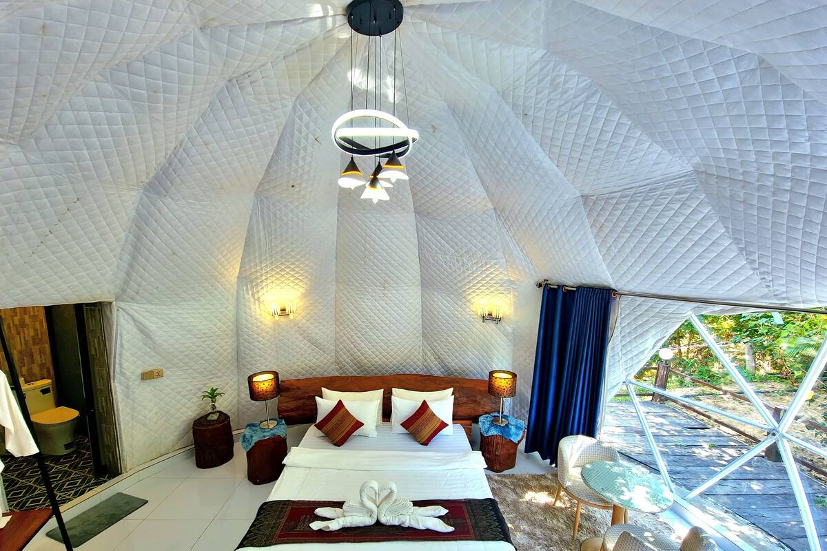 A spacious tented accommodation with a large bed, bedside lamps, and a view of the outdoors.