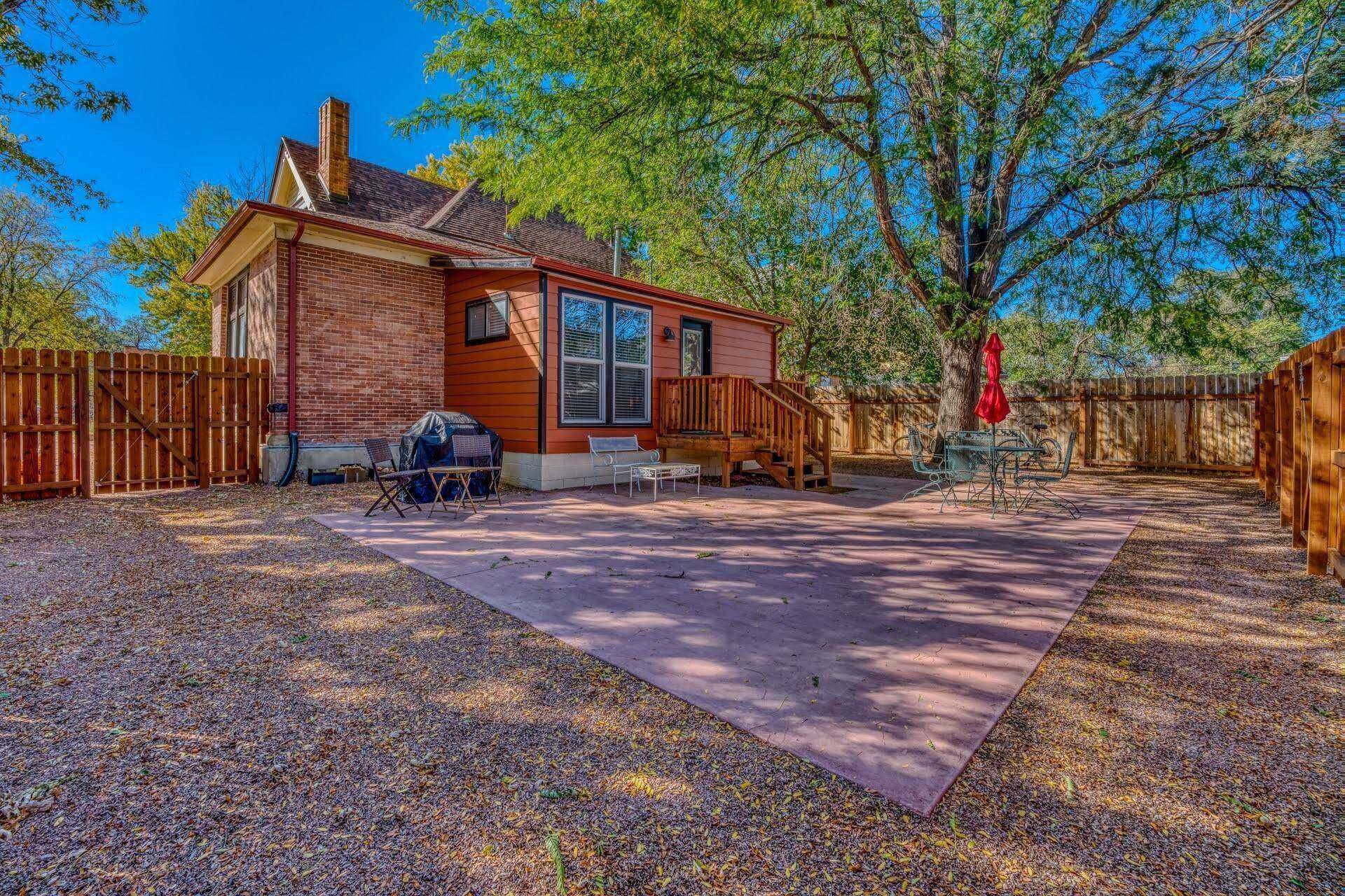 A single-story brick house with a covered patio, a wooden deck, and a fenced backyard.