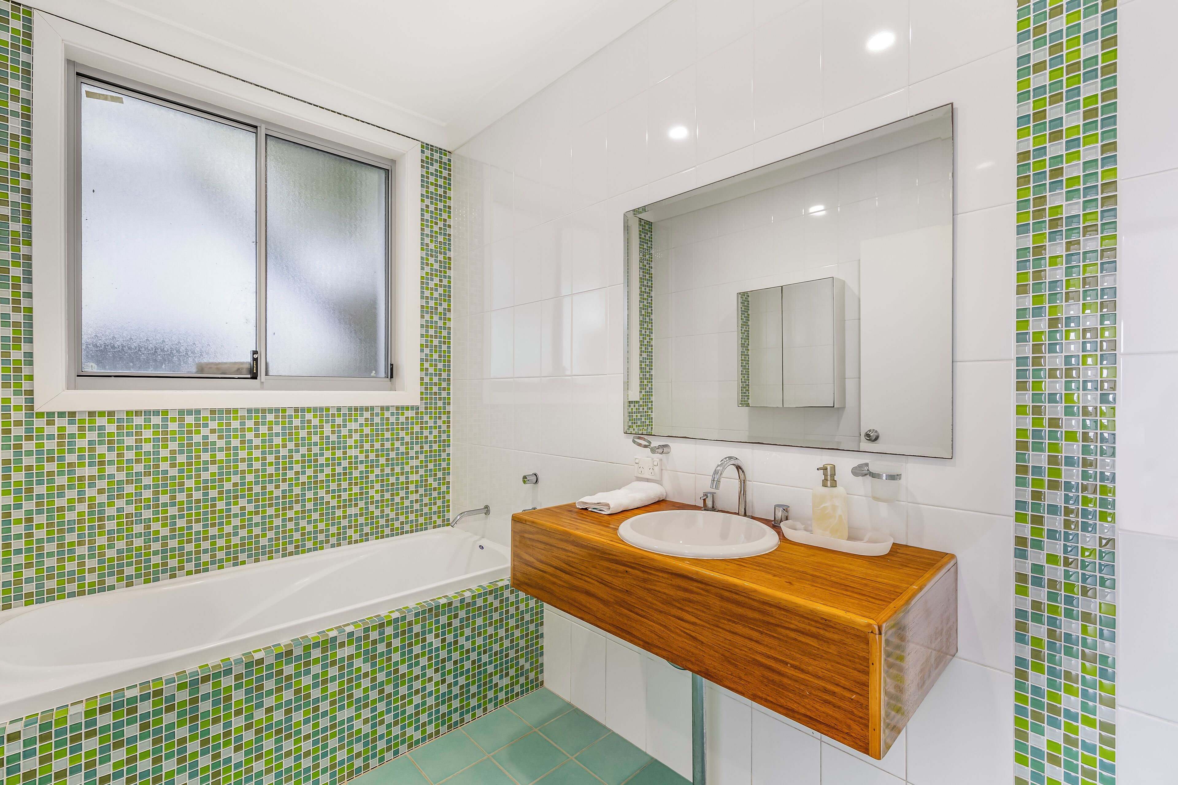 A bathroom with a wooden vanity, a white sink, and a large mirror.