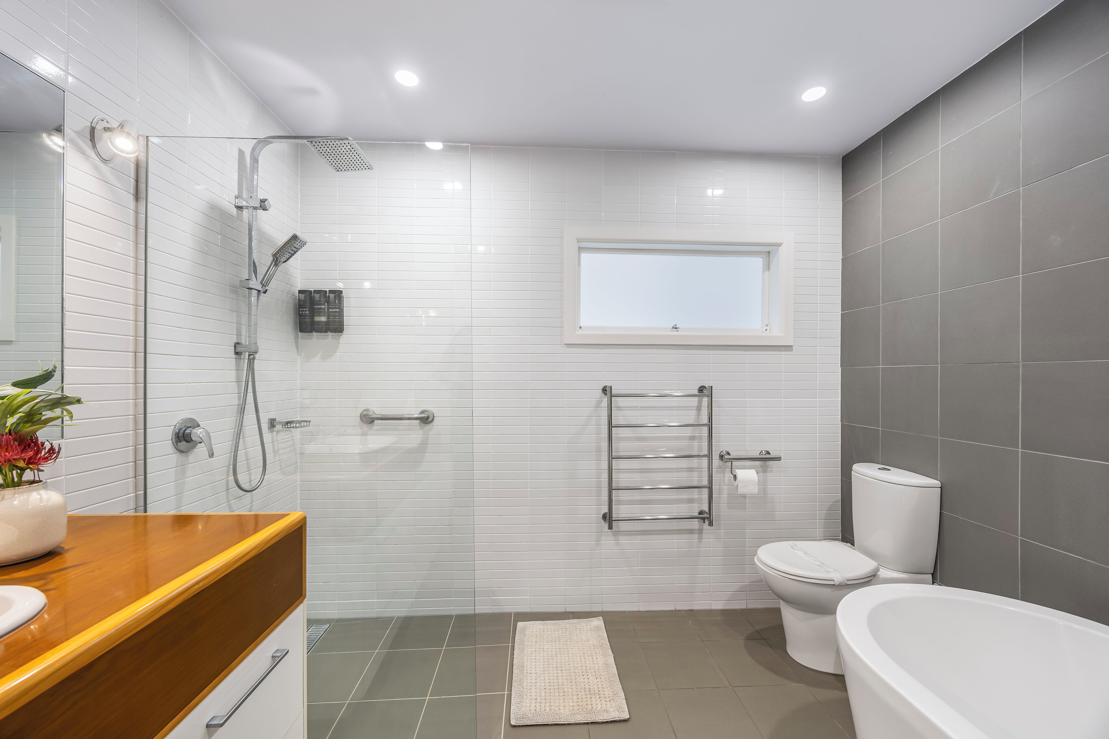 Een moderne badkamer met een douchecabine van glas, een toilet, een badkuip en een wastafel met spiegel.