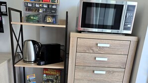 Una kitchenette con microondas, tetera y estantes con frascos y libros.