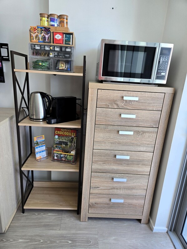 A kitchenette with a microwave, kettle, and shelves with jars and books.