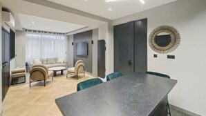 Una sala moderna con una mesa de comedor y sillas, un conjunto de sofás y un televisor montado en la pared.