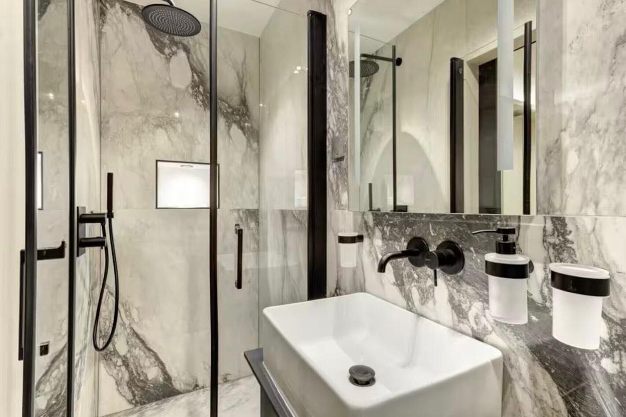 Ein modernes Badezimmer mit einer gläsernen Duschkabine, einem weißen Waschbecken und einem großen Spiegel.