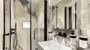 Un baño moderno con ducha envuelta en vidrio, un lavamanos blanco y un espejo grande.