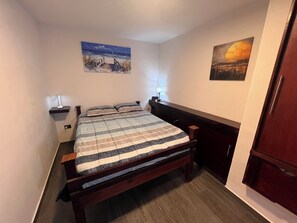 Een slaapkamer met een houten bed, een nachtkastje, een lamp en twee aan de muur hangende schilderijen.