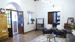 A spacious living room with a wooden floor, a large arched doorway, a chandelier, and a traditional wooden chair. - West Berry Vintage (Ootacamund)