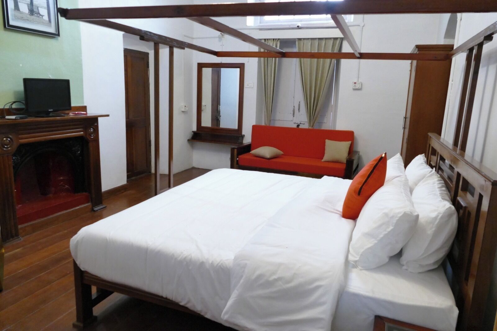 Un dormitorio con una cama grande, un escritorio de madera con una computadora, un sofá rojo y una ventana con cortinas.