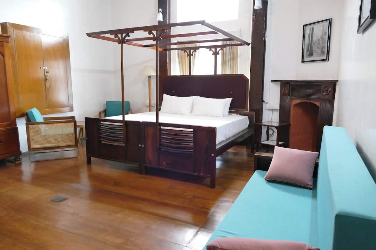 Ein traditionell eingerichteter Raum mit Himmelbett, Holzschrank, Rattan-Sessel und einem blaugrünen Sofa.