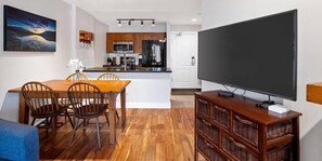 Una cocina moderna con armarios de madera, un comedor con mesa y sillas de madera, y un televisor de pantalla plana grande montado en la pared.