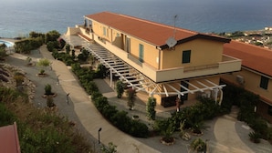 A building with a red-tiled roof, a covered outdoor area with a pergola, and a view of the sea.