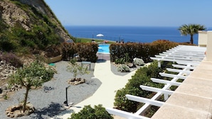 A pool area with a view of the ocean, surrounded by greenery and white pergolas.