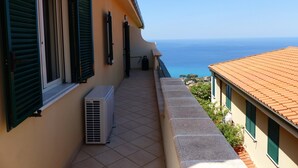 A balcony with a view of the sea, a tiled floor, and a building with green shutters.