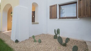 A building with white walls, wooden shutters, and a window. There are cacti in the foreground. - Eucaliptos Apartment Porto Cervo (Porto Cervo)