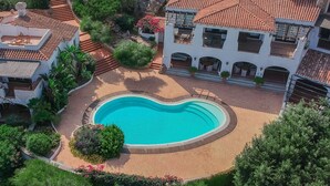 A pool surrounded by a garden, a building with a tiled roof, and a stone staircase. - Alba Apartments in Porto Cervo (Porto Cervo)