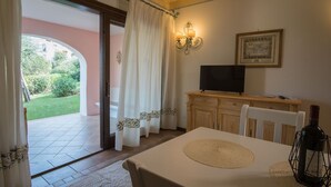 A room with a dining table, chairs, a television on a wooden cabinet, and a framed picture on the wall. - La Vela Apartments in Porto Cervo (Porto Cervo)