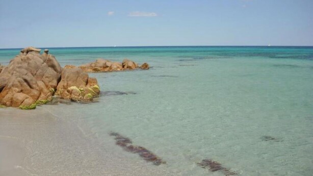 Una playa con agua turquesa cristalina y grandes rocas al frente.