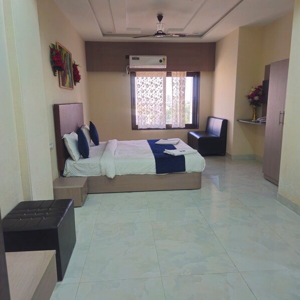 A hotel room with a bed, a desk, a chair, and an air conditioning unit. - Hotel Lord Krishna Dham (Dwarka)