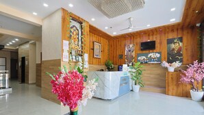 A hotel reception area with a wooden reception desk, a marble counter, and a ceiling fan. - Hotel Lord Krishna Dham (Dwarka)