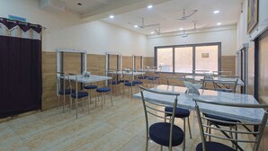 A dining area with multiple tables and chairs, ceiling fans, and a large window. - Hotel Lord Krishna Dham (Dwarka)