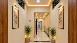 A corridor with marble flooring, framed wall art, and potted plants. - Hotel Lord Krishna Dham (Dwarka)