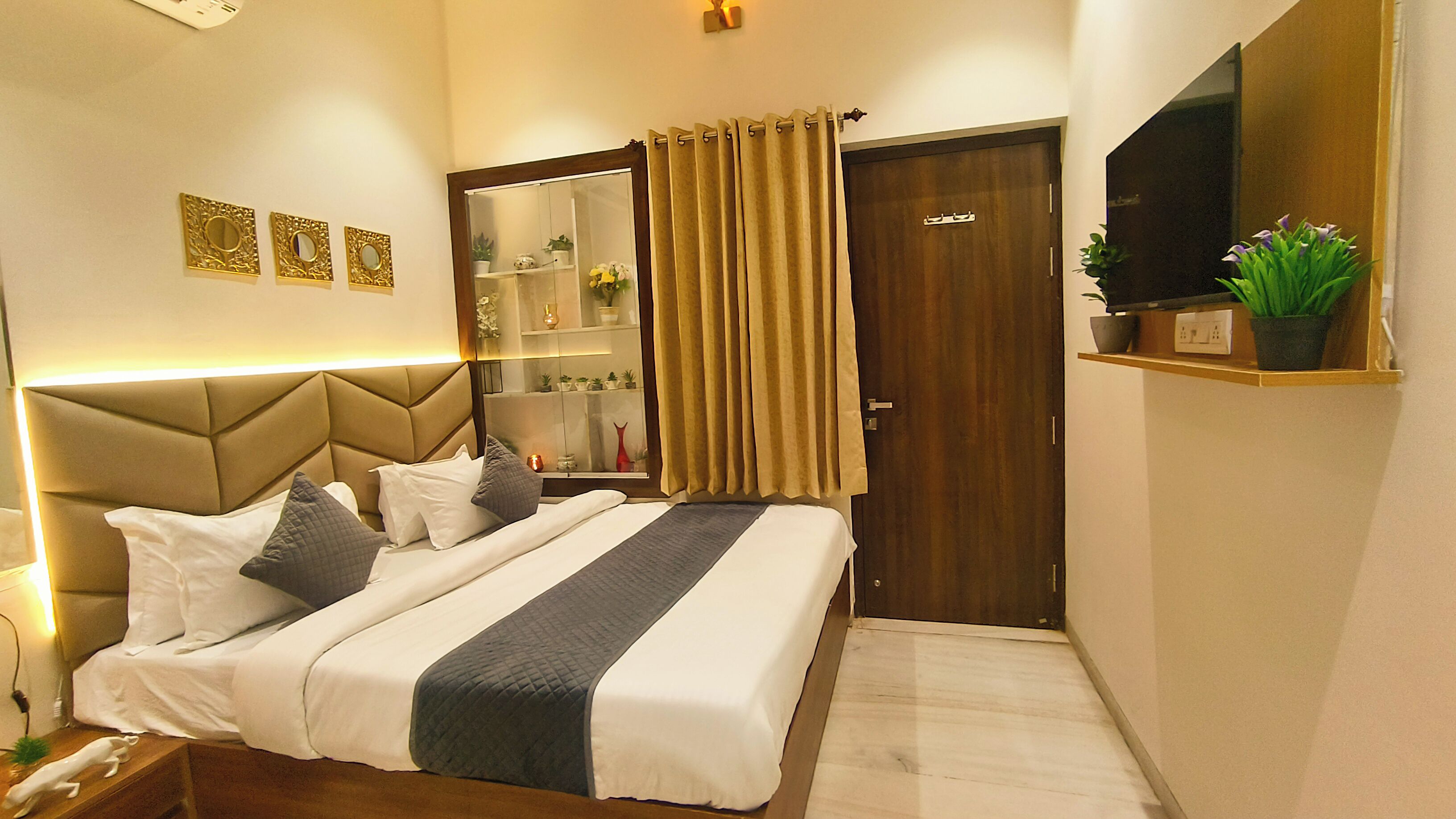 Une chambre d’hôtel comprenant un lit, une table de chevet, une commode, un miroir, une armoire et une étagère avec des plantes.