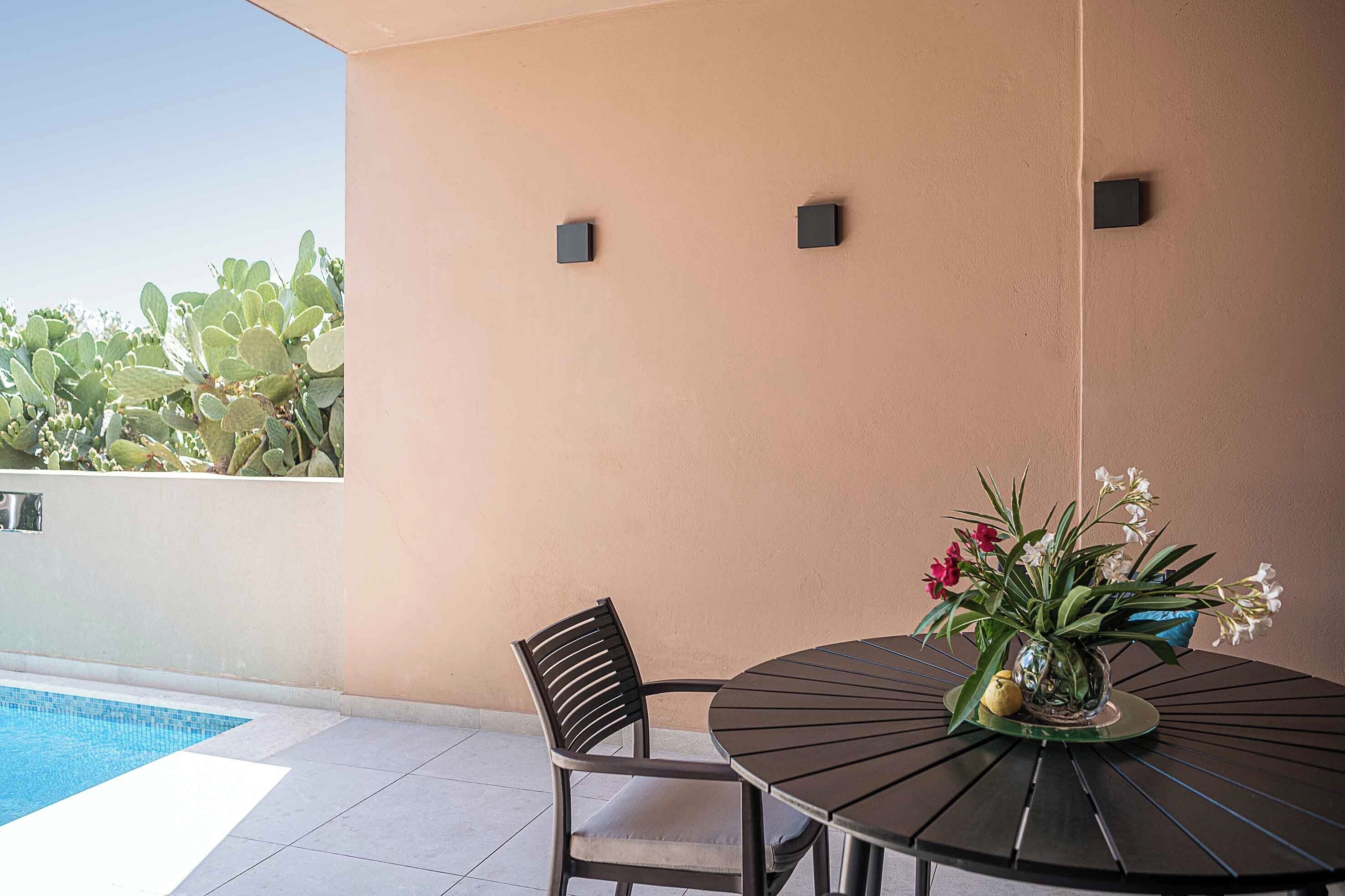 A patio area with a round table and two chairs, a small pool, and a wall with a cactus garden.
