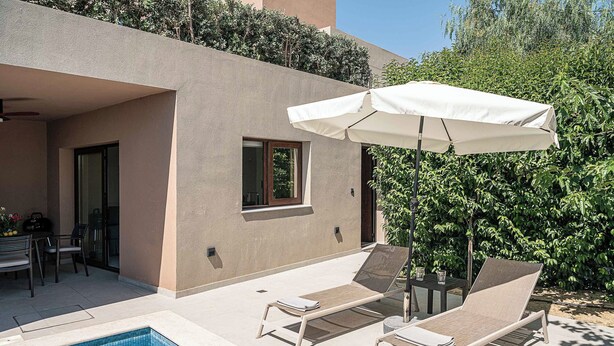 Un área junto a la piscina con sillones de descanso y una mesa, un porche cubierto y vistas a un edificio con una ventana.