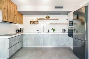 A modern kitchen with a built-in refrigerator, a coffee maker, and a kettle on the counter. - Villa Fos | Private pool, elegance & seaview! (Crete)
