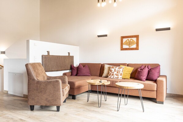 A modern living room with a brown sofa, a brown armchair, and two round wooden side tables. - Superior Ferienhaus # 4A mit Sauna (Uttendorf)