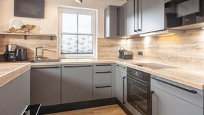 A modern kitchen with grey cabinetry, a wooden countertop, a built-in oven, and a window with blinds. - Superior Ferienhaus # 4A mit Sauna (Uttendorf)
