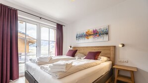 A bedroom with a large bed, a wooden headboard, a small bedside table, and a window with curtains. - Superior Ferienhaus # 4A mit Sauna (Uttendorf)