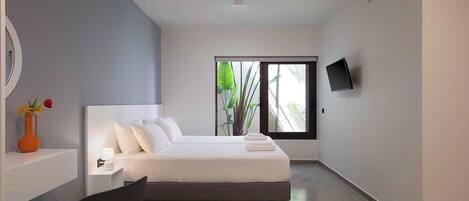 Une chambre d’hôtel moderne équipée d’un lit, d’une chaise, d’un bureau avec un vase, d’une télévision et d’une fenêtre donnant sur un paysage verdoyant.