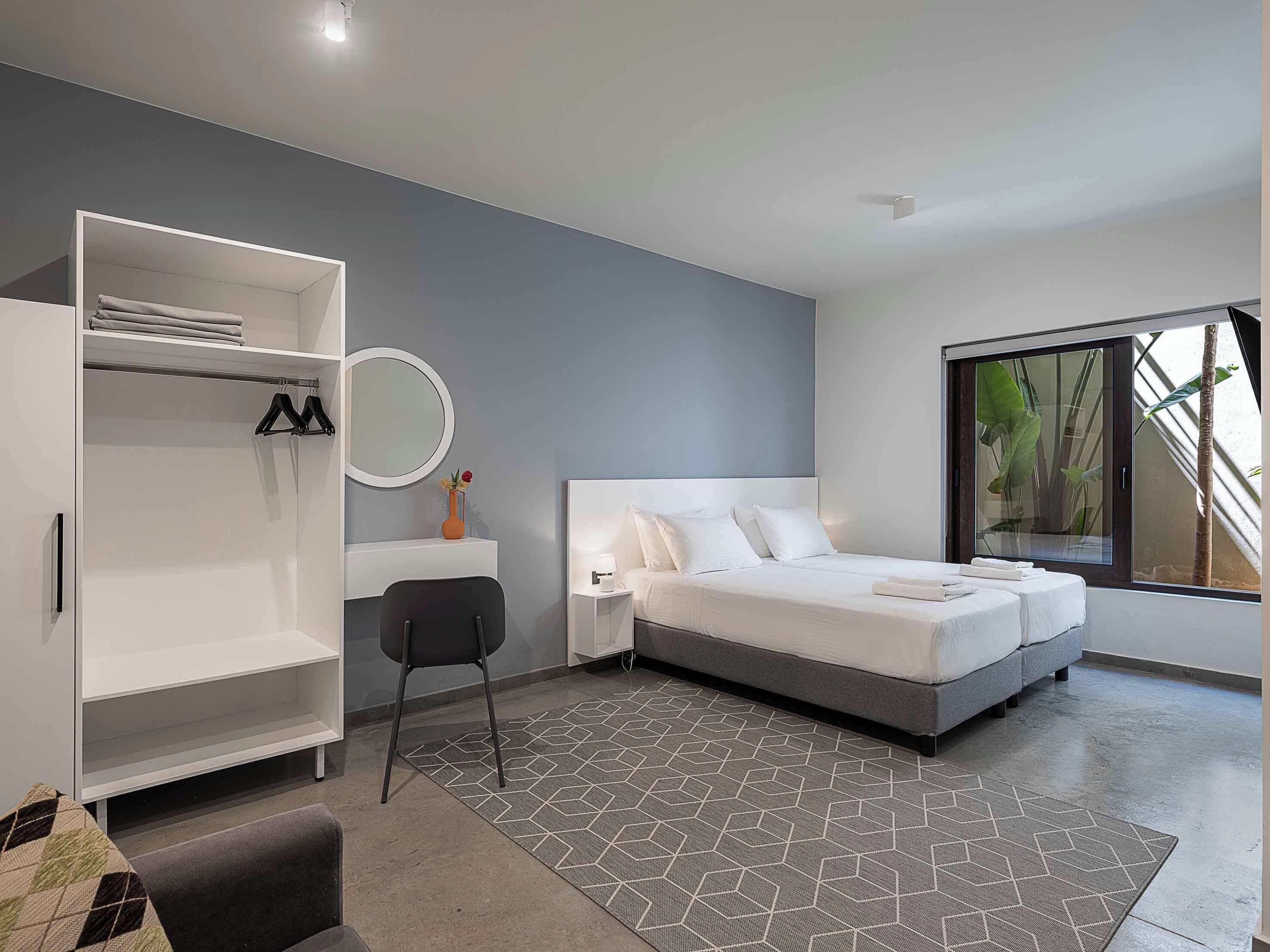 A modern bedroom with a bed, a wardrobe, a desk, and a large window.