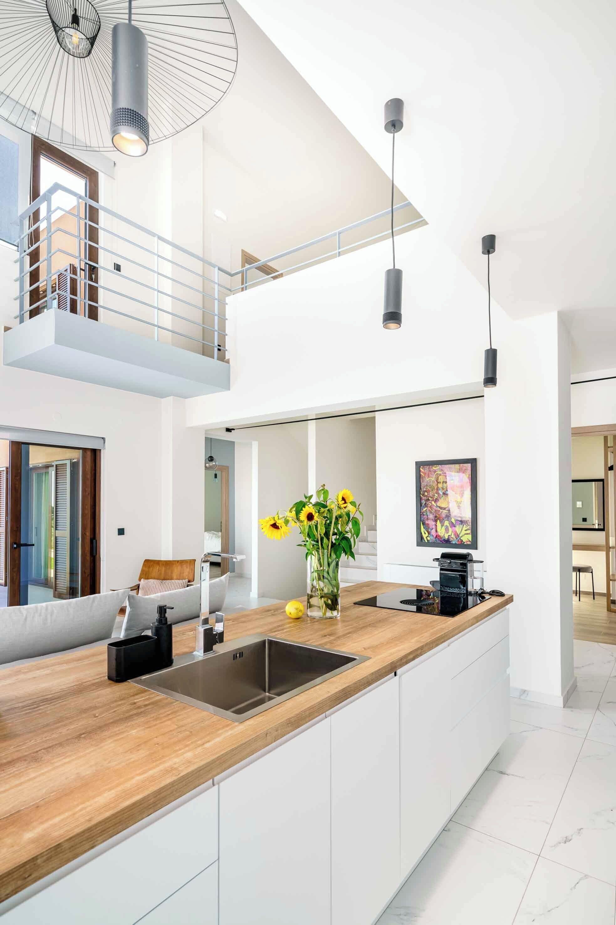 A modern kitchen with a wooden countertop, stainless steel sink, and pendant lighting.