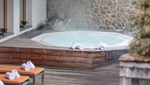 A hot tub with towels, a wooden deck, and a stone wall.