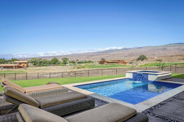 Piscina con cascada, rodeada de sillas de descanso y vistas a colinas distantes.