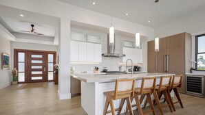 Una cocina moderna con una isla central, taburetes de madera, iluminación colgante y electrodomésticos de acero inoxidable.