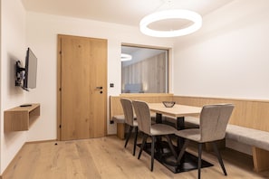 A modern dining area with a wooden table, four chairs, a bench, a TV mounted on the wall, and a wooden door.