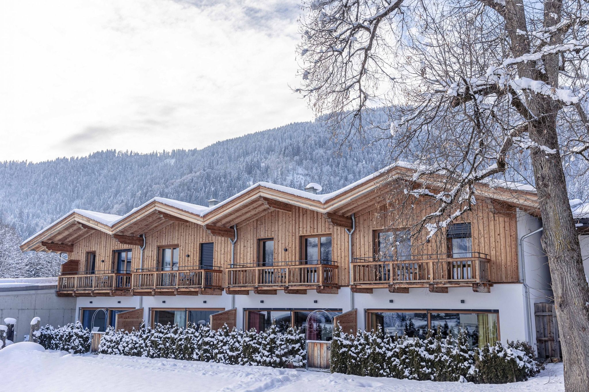 A wooden chalet with multiple balconies, large windows, and a snowy mountain backdrop.