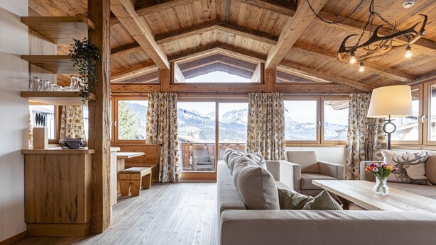 Un interior de madera acogedor con sofá, zona de comedor y ventanas amplias con vistas a las montañas.