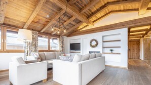 Una sala de estar moderna con techo de madera, un conjunto de sofás, un televisor y una chimenea.