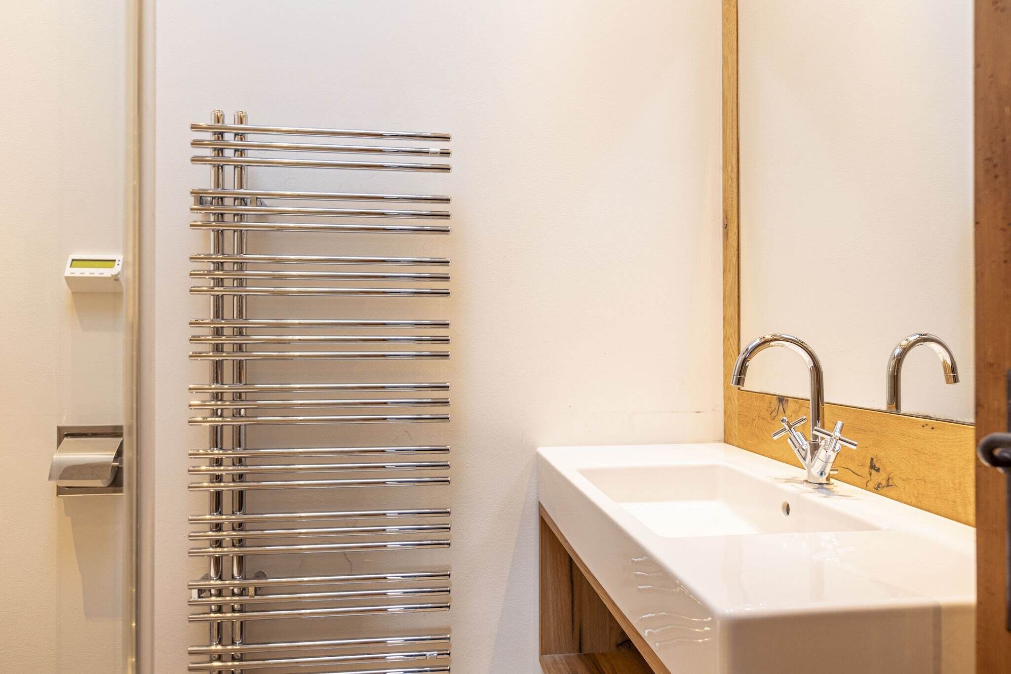 Un baño moderno con un perchero cromado, un lavabo blanco y un espejo con marco de madera.