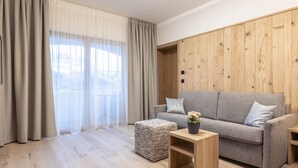 A modern living room with a grey sofa, wooden panel wall, and a large window with sheer curtains.