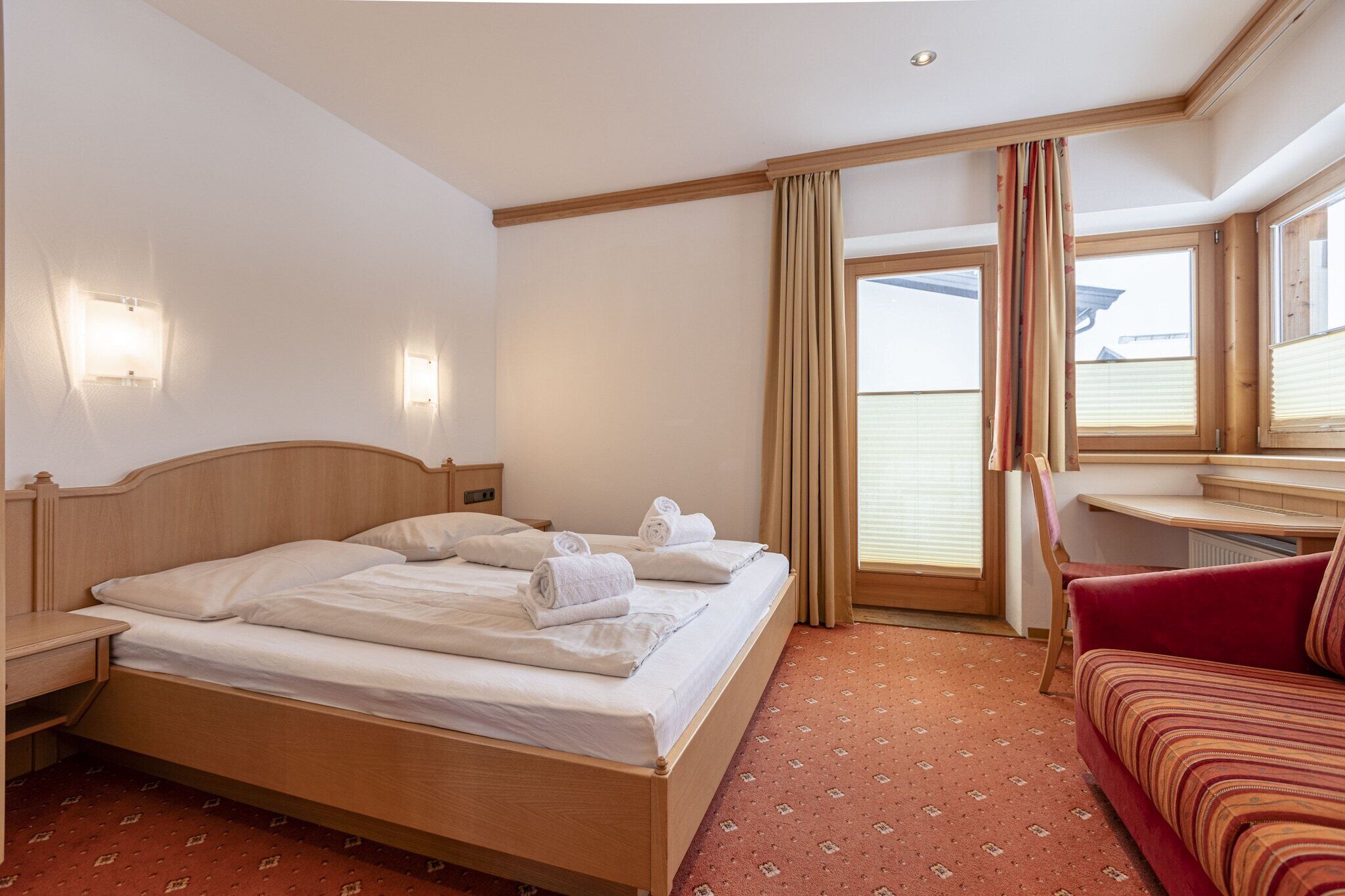 Een hotelkamer met een houten bed, een rode bank, een bureau en een raam met gordijnen.