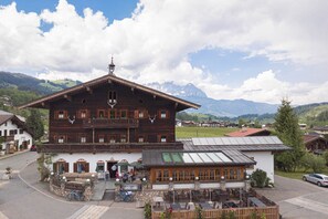 A traditional wooden building with a balcony, a stone foundation, and a restaurant area with outdoor seating.