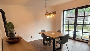 A dining area with a wooden table and chairs, a hanging light fixture, and a view through large windows. - Vacation apartment Am Kreuzberg Apartment No. 3 (Nordrhein-Westfalen - Schleiden)